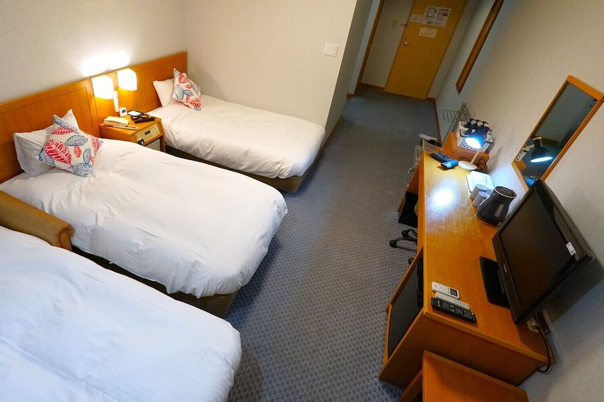 A hotel room with two beds, a desk with a computer and phone, and a mirror.