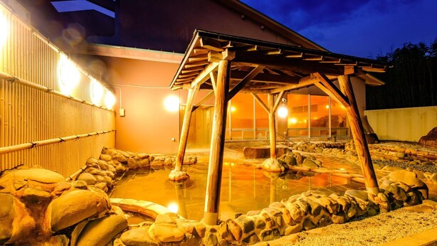 Un onsen japonés tradicional con una estructura de baños de madera, asientos de piedra y vistas despejadas al área de aguas termales.