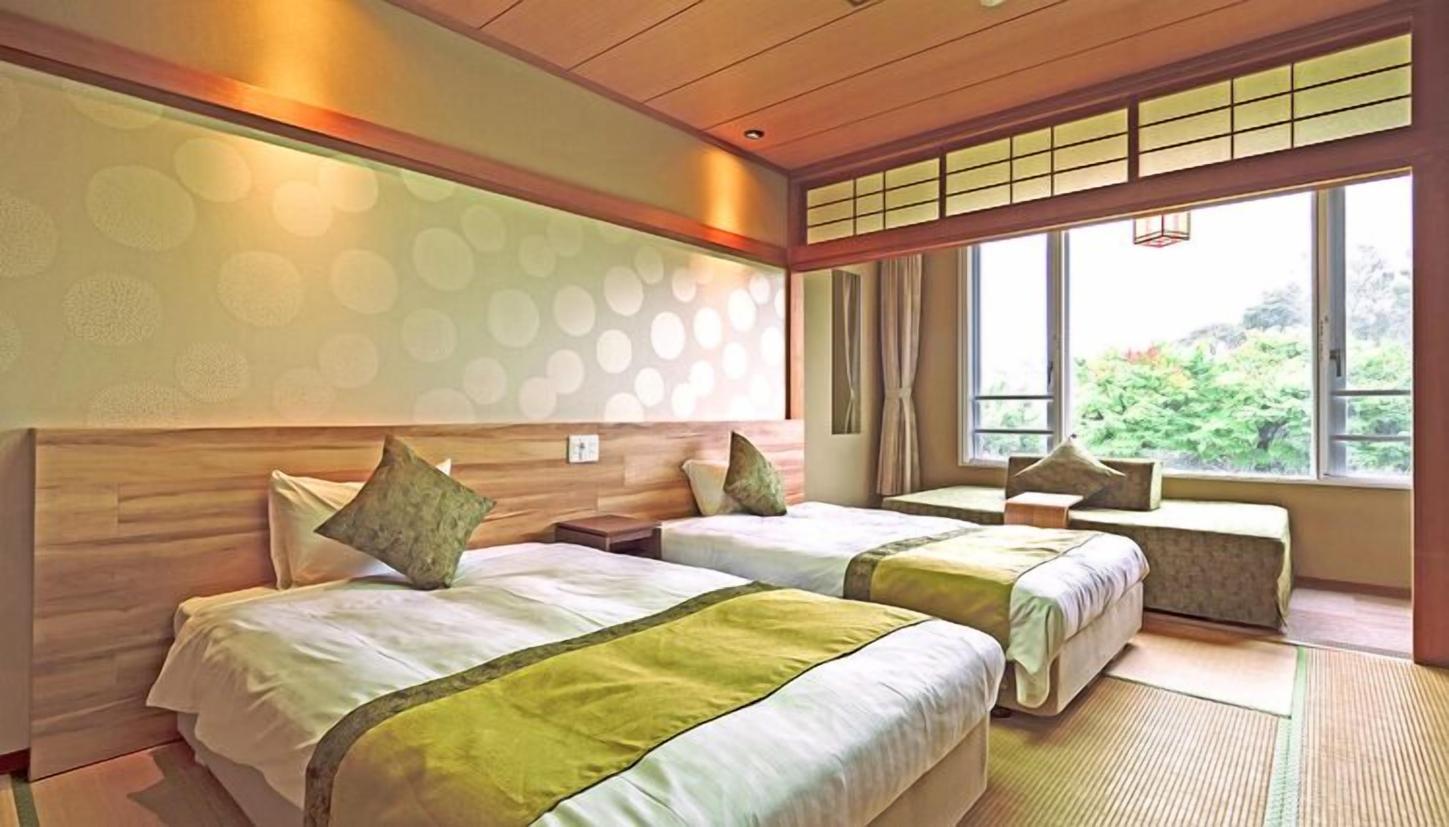 A hotel room with two beds, a large window, and a view of greenery.