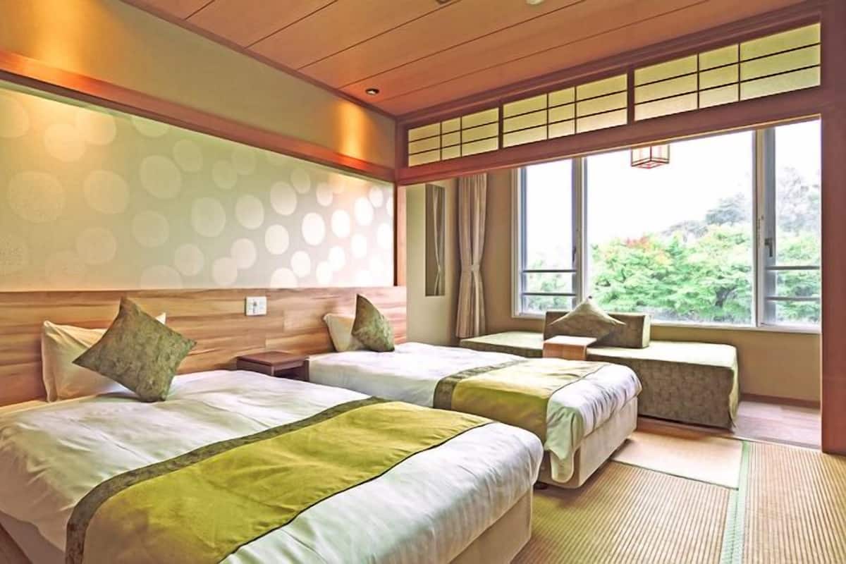 A hotel room with two beds, a large window, and a view of greenery.