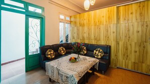 Un salon chaleureux avec un mur en bois, une porte à cadre vert, un canapé en cuir noir et une nappe à motifs.