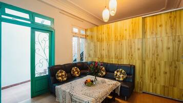 Uma sala de estar aconchegante com parede de madeira, porta com moldura verde, sofá de couro preto e toalha de mesa estampada.