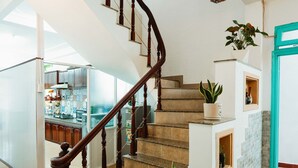 Un escalier avec des balustres en bois et une main courante, menant à un palier où se trouve un pot de fleurs.