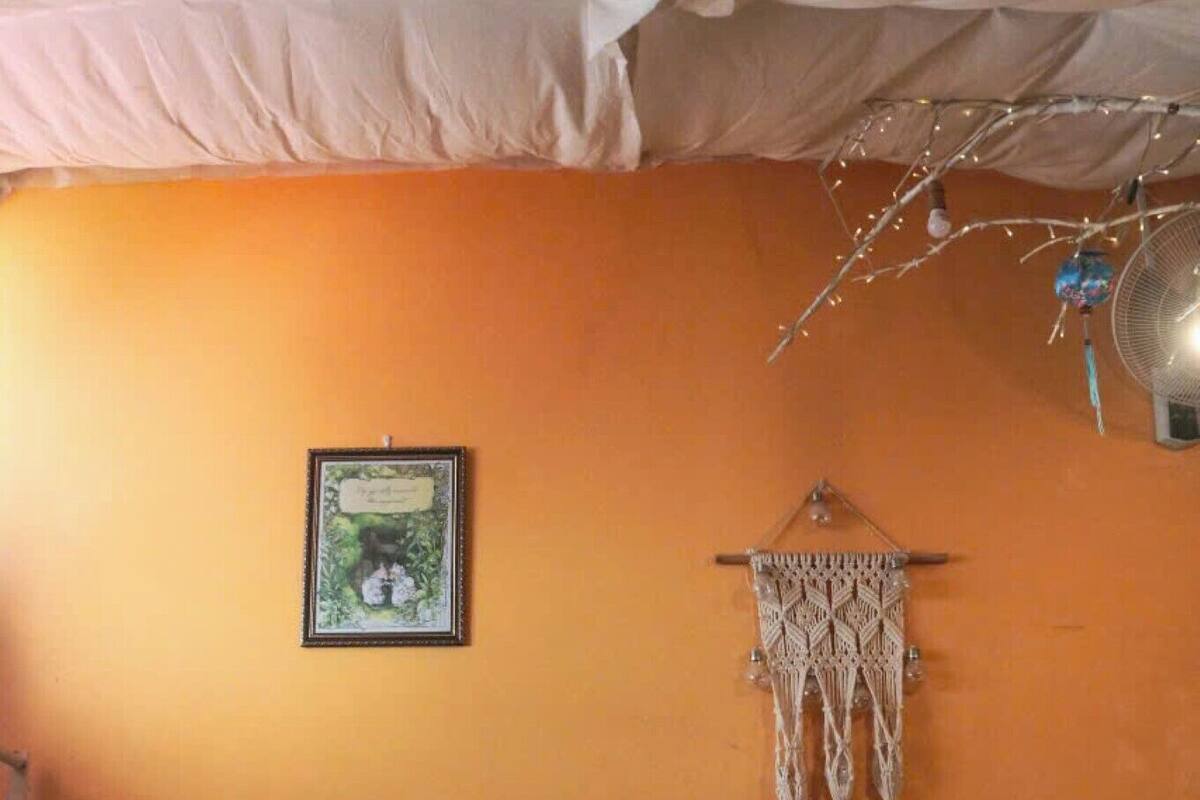 A bedroom with a bed, a macrame wall hanging, and a framed picture on the wall.