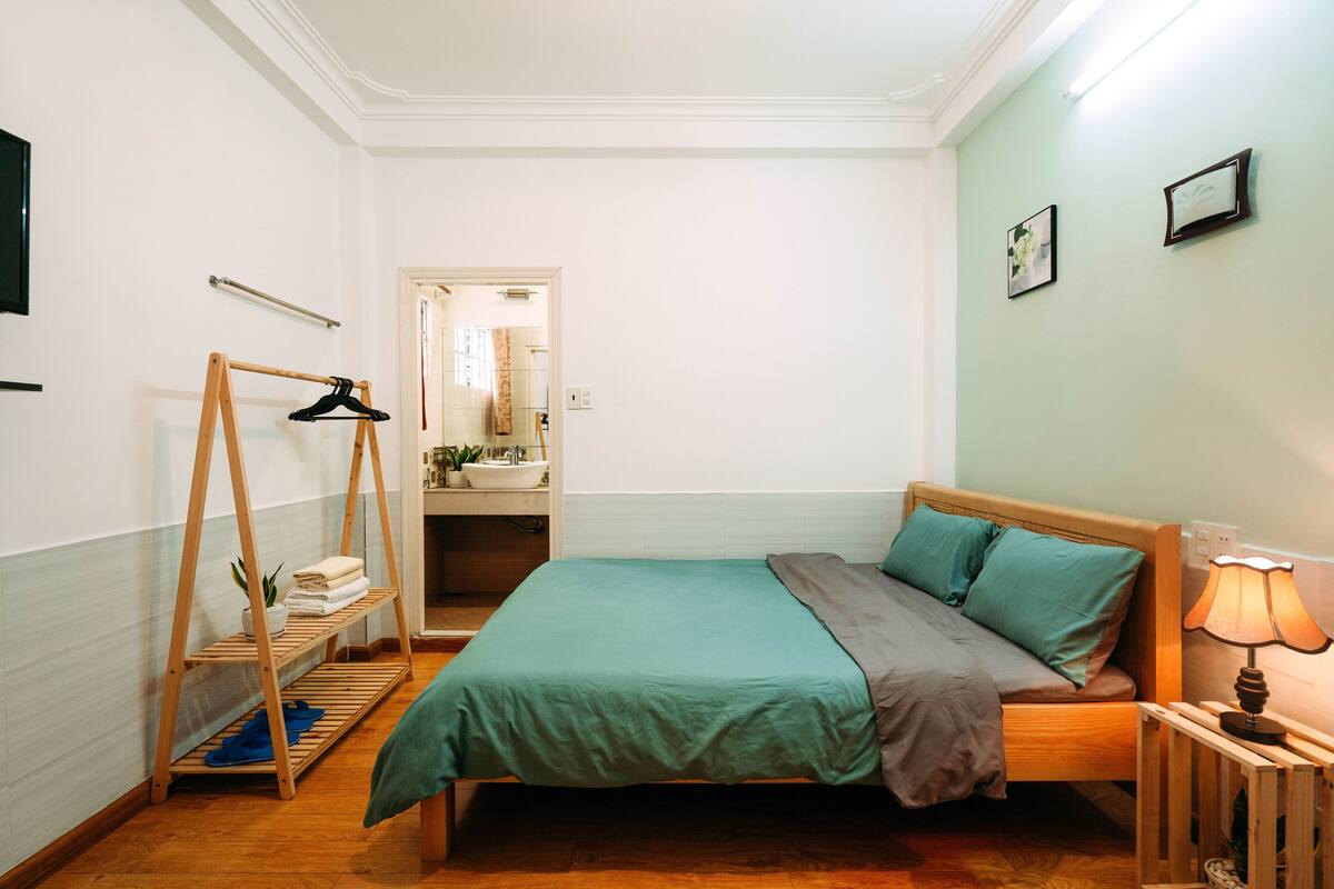 A neatly arranged bedroom with a bed, bedside lamp, and a wooden hanger rack with towels.