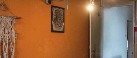 Una habitación con pared naranja, una cama con edredón estampado, un colgador de macramé, un ventilador y un marco de fotos.