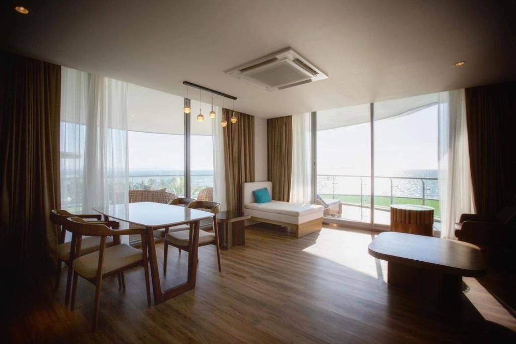 A modern hotel room with a dining area, a sofa, and large windows offering a view.