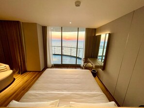 Een hotelkamer met een groot bed, een bureau en uitzicht op de zee door middel van kamerhoge ramen.