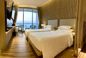 Ein Hotelzimmer mit zwei Betten, einem Fernseher, einem Schreibtisch und Meerblick.