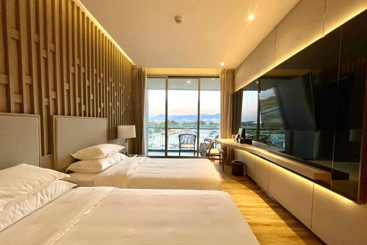 Ein modernes Hotelzimmer mit zwei Betten, einem großen Fernseher und einem Balkon mit Blick auf die Stadt.