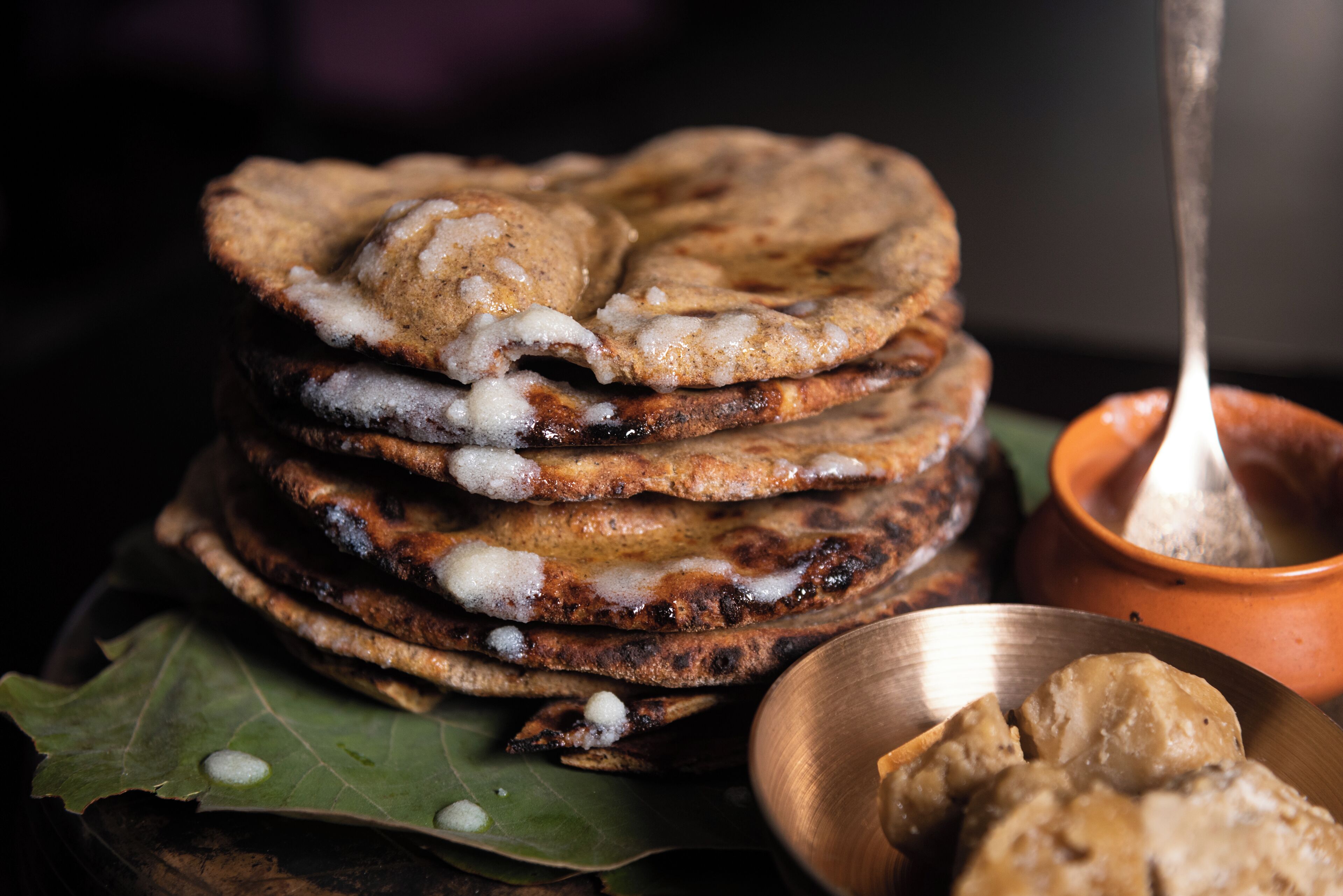 A stack of flatbreads with a dipping sauce, served on a leaf and a metal plate.