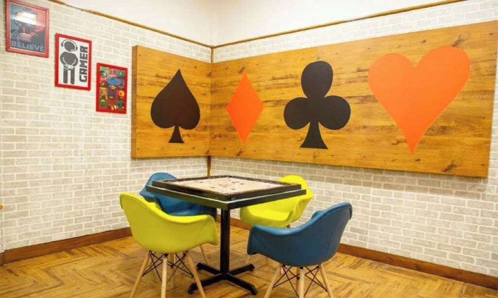 A room with a wooden partition displaying playing card symbols, a table with chairs, and a brick wall.