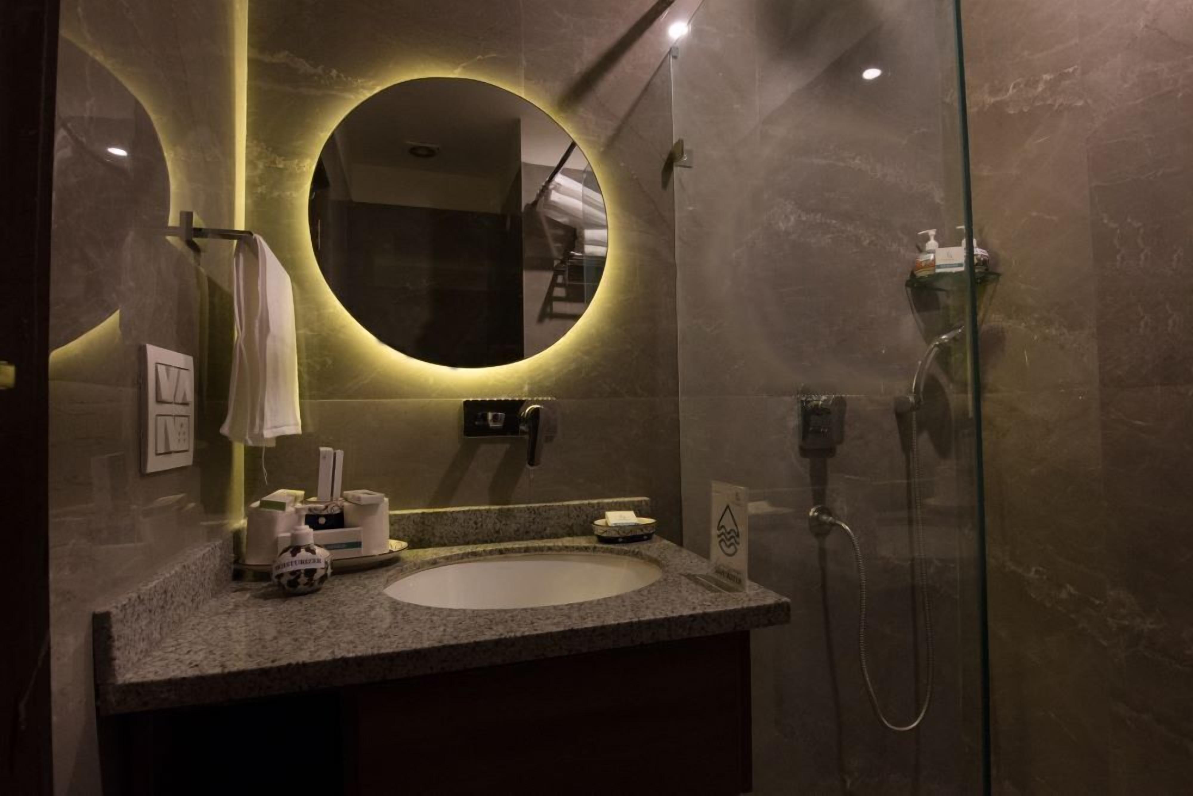 A modern bathroom with a round mirror, a sink, and a glass-enclosed shower.
