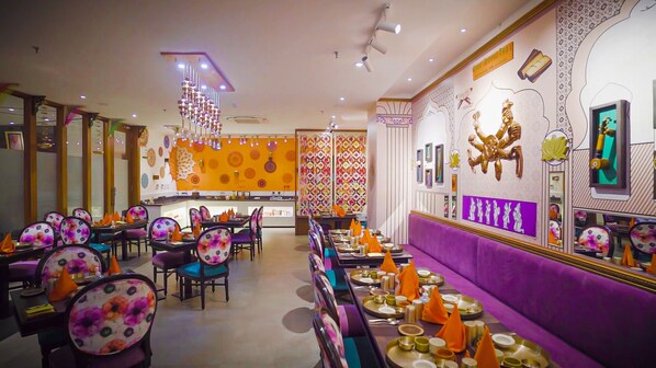 Ein Restaurant mit lebendiger Einrichtung, das eine zentrale Bar, mehrere Essplätze mit Stühlen und eine Wand mit kultureller Kunst bietet.