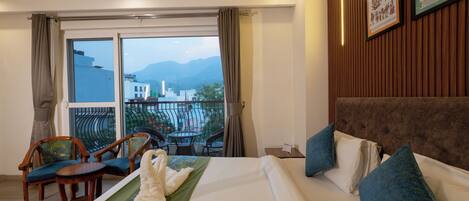 Habitación de hotel con cama, balcón con sillas y vista a las montañas.