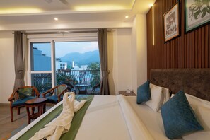 A hotel room with a bed, a balcony with chairs, and a view of mountains. - HOLYWATER Hotel by Ganga Kinare (150 mts from Ganga Ghat) (Rishikesh)