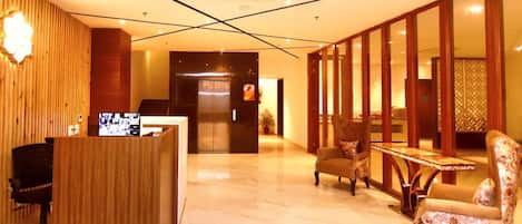 A hotel lobby with a reception desk, seating area, and a large mirror reflecting the interior.
