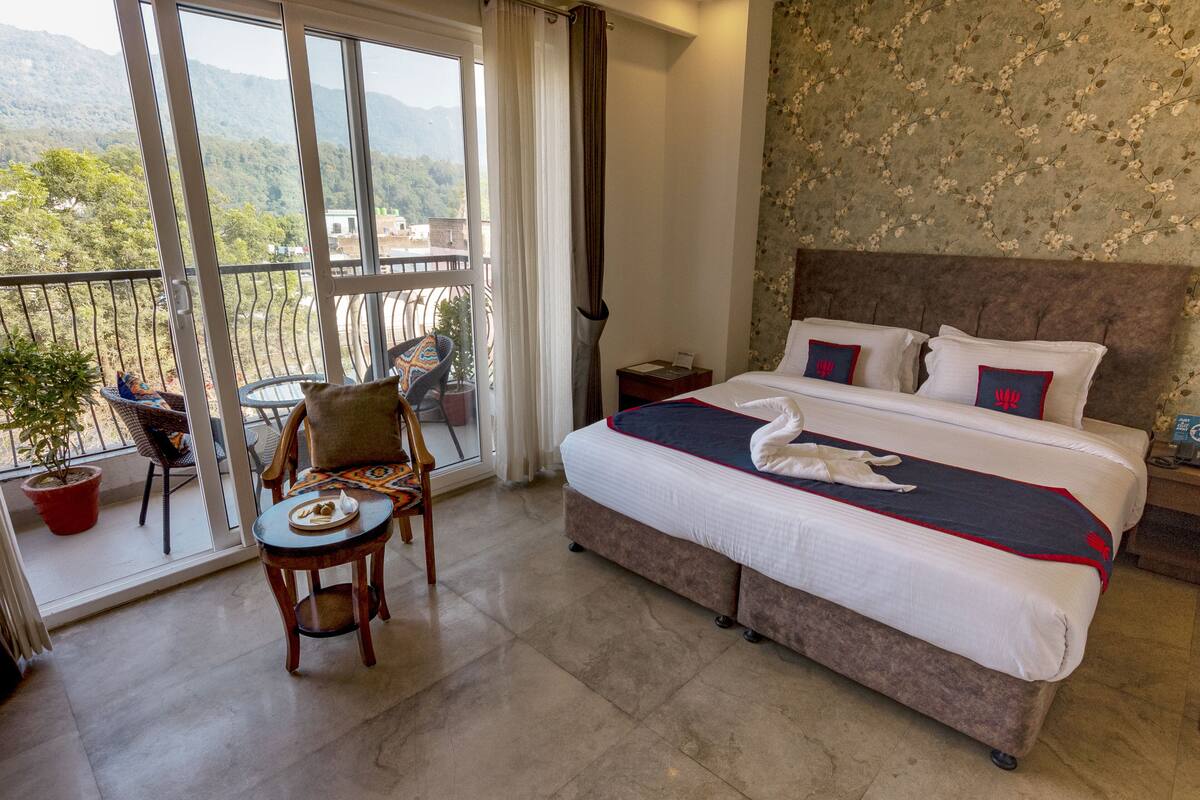 Une chambre d’hôtel avec un grand lit, un balcon équipé d’une chaise et d’une table, et une vue sur les montagnes.