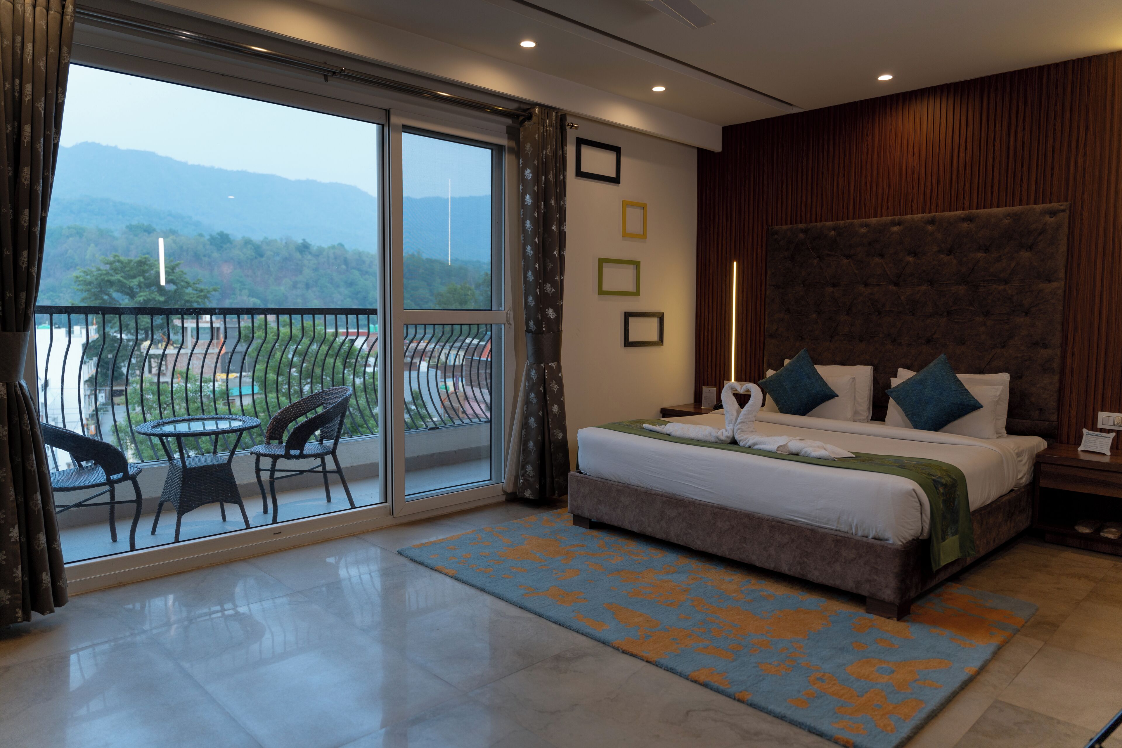 Un dormitorio con una cama grande, un balcón con sillas y vistas a montañas.