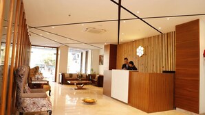 Een hotel receptie met een houten balie, een receptionist en een zithoek met een bank en fauteuils.