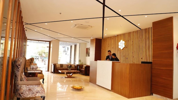 Ein Hotel-Empfangsbereich mit einem Holzbüro, einer Rezeptionistin und einer Sitzecke mit einer Couch und Sesseln.