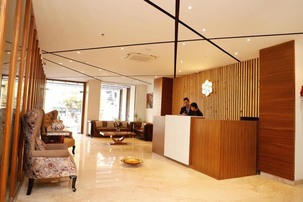 Een hotel receptie met een houten balie, een receptionist en een zithoek met een bank en fauteuils.