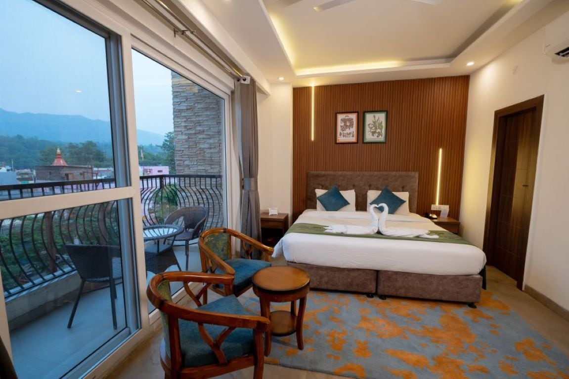 A hotel room with a large bed, a balcony with chairs, and a view of the mountains.