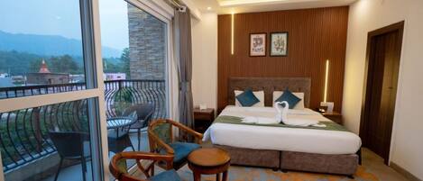 A hotel room with a large bed, a balcony with chairs, and a view of the mountains.