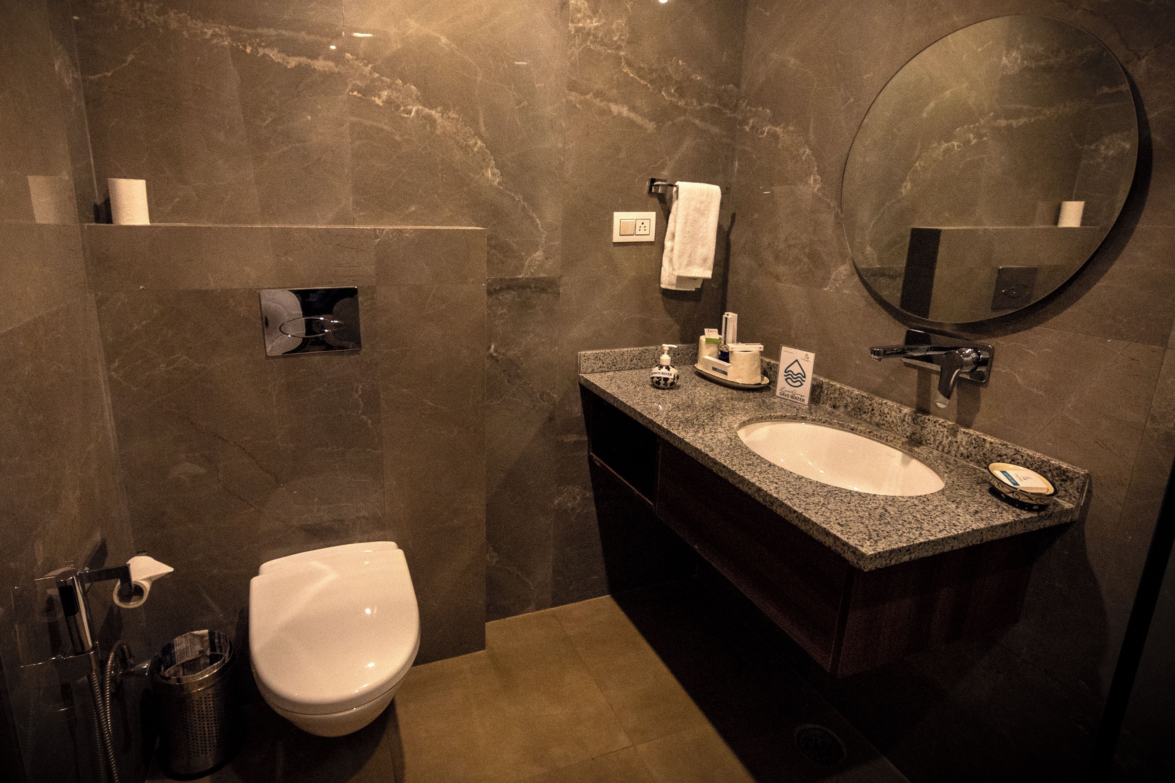 Un bagno moderno con parete in marmo, vaso bianco, lavabo in granito e uno specchio grande.