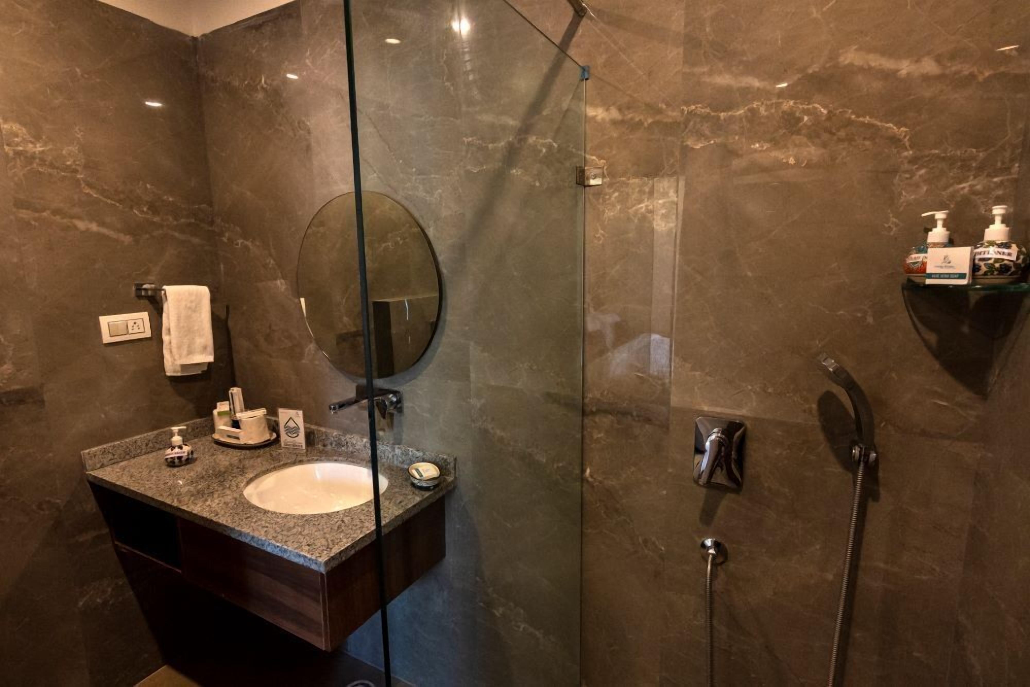 Un bagno moderno con lavabo su piano in granito, cabina doccia in vetro e parete in marmo.