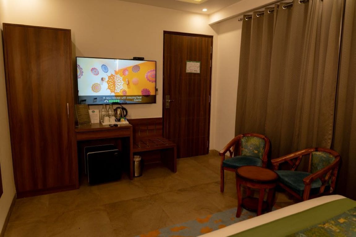A hotel room with a television, a desk with a coffee maker, two chairs, and a bed.
