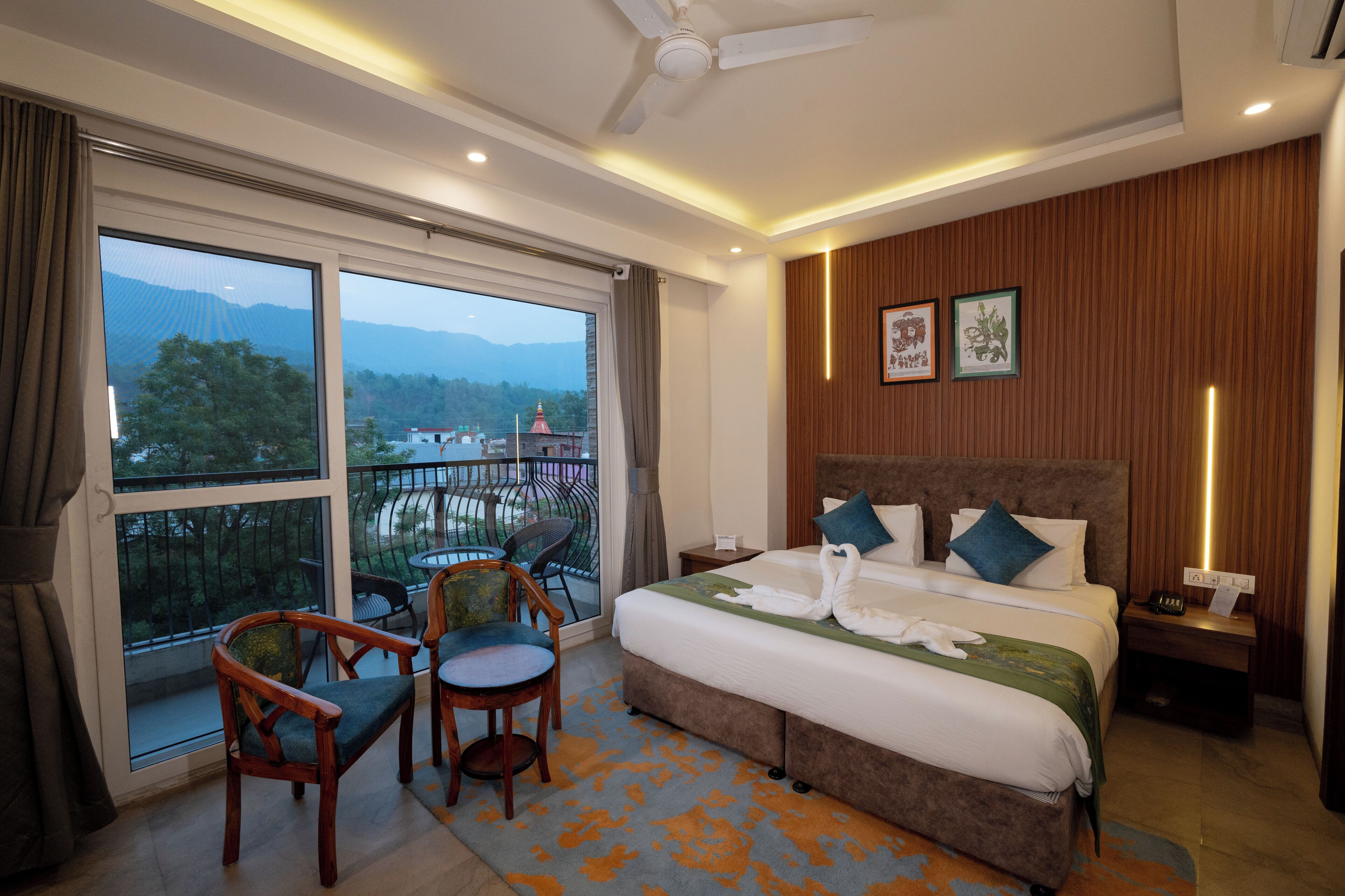 A hotel room with a large bed, two chairs, a nightstand, and a view of mountains through the window.