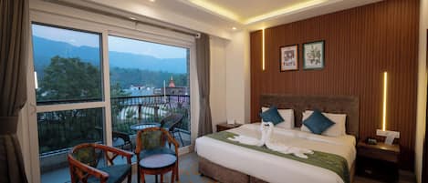 A hotel room with a large bed, two chairs, a nightstand, and a view of mountains through the window.