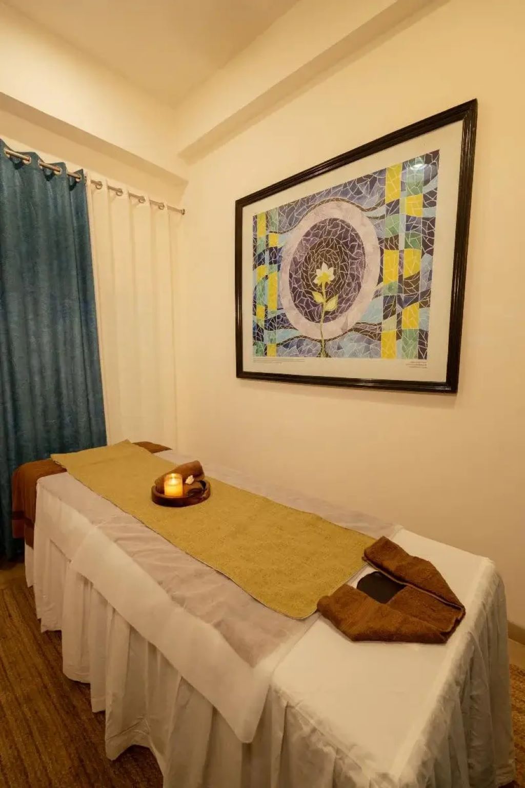 A room with a massage table, a framed artwork, and a window with curtains.