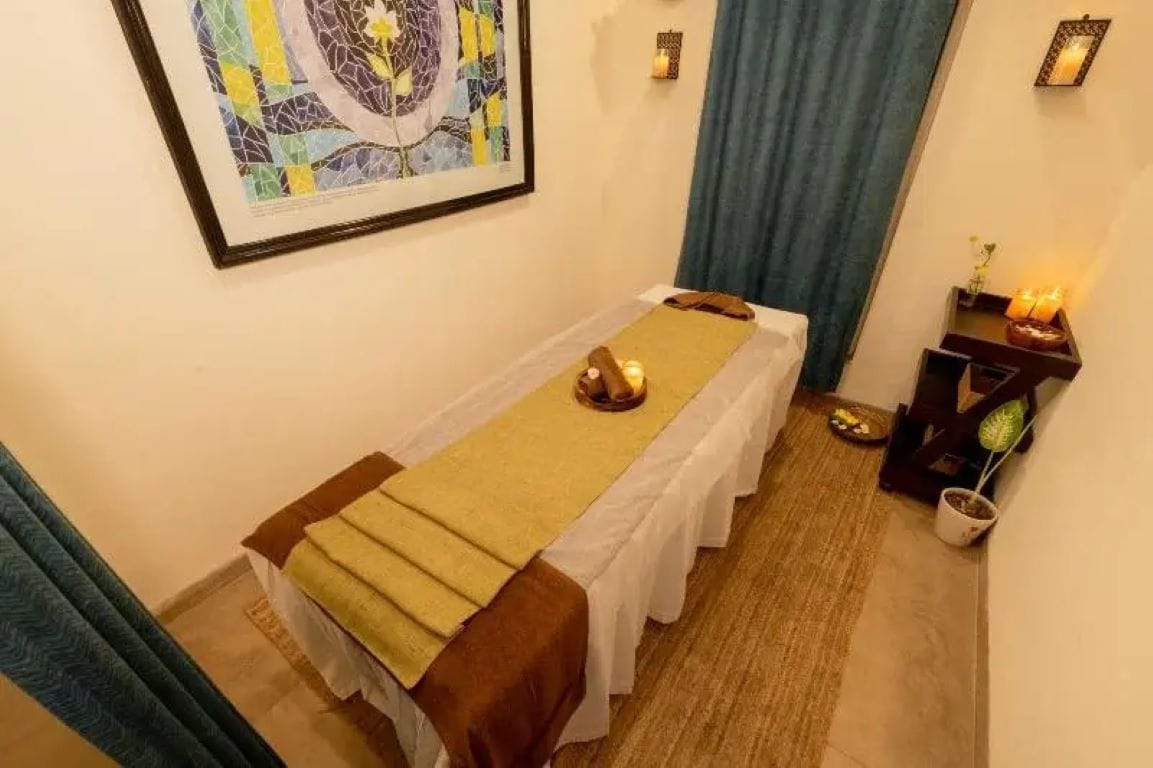 A massage therapy room with a bed, a small table with candles, and a framed artwork on the wall.