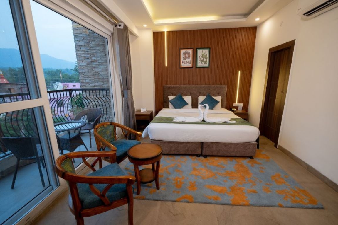 A hotel room with a bed, a balcony with chairs, and a view of the outside.