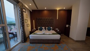 Een hotelkamer met een groot bed, een balkon met een stoel en uitzicht op de bergen.