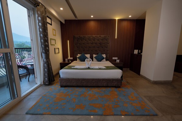 Een hotelkamer met een groot bed, een balkon met een stoel en uitzicht op de bergen.