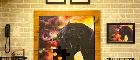A wall with a large jigsaw puzzle artwork of a buffalo, framed and hung on a brick wall.
