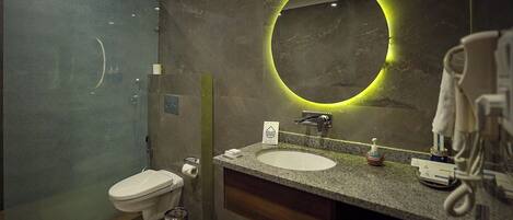 A modern bathroom with a glass shower enclosure, a white sink, and a round mirror with a green light.