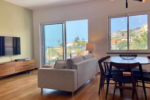 Una sala de estar moderna con un sofá, una mesa de comedor y sillas, ventanas amplias con vistas a un paisaje montañoso.