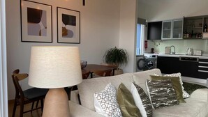 Ein modernes Wohnzimmer mit einer Couch, einem Esstisch, Stühlen, einer Lampe und einer Küchenzeile mit Geräten.