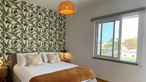 Ein Schlafzimmer mit einem Bett, einem Fenster mit Ausblick, einer Wand mit Muster und einer hängenden Leuchte.