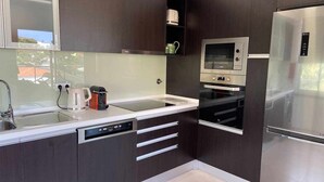 Eine moderne Küche mit dunklen Schränken, einem Edelstahl-Kühlschrank, einem eingebauten Backofen und einem Geschirrspüler.