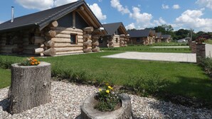 A row of log cabins with a paved walkway and a grassy area with flowers.