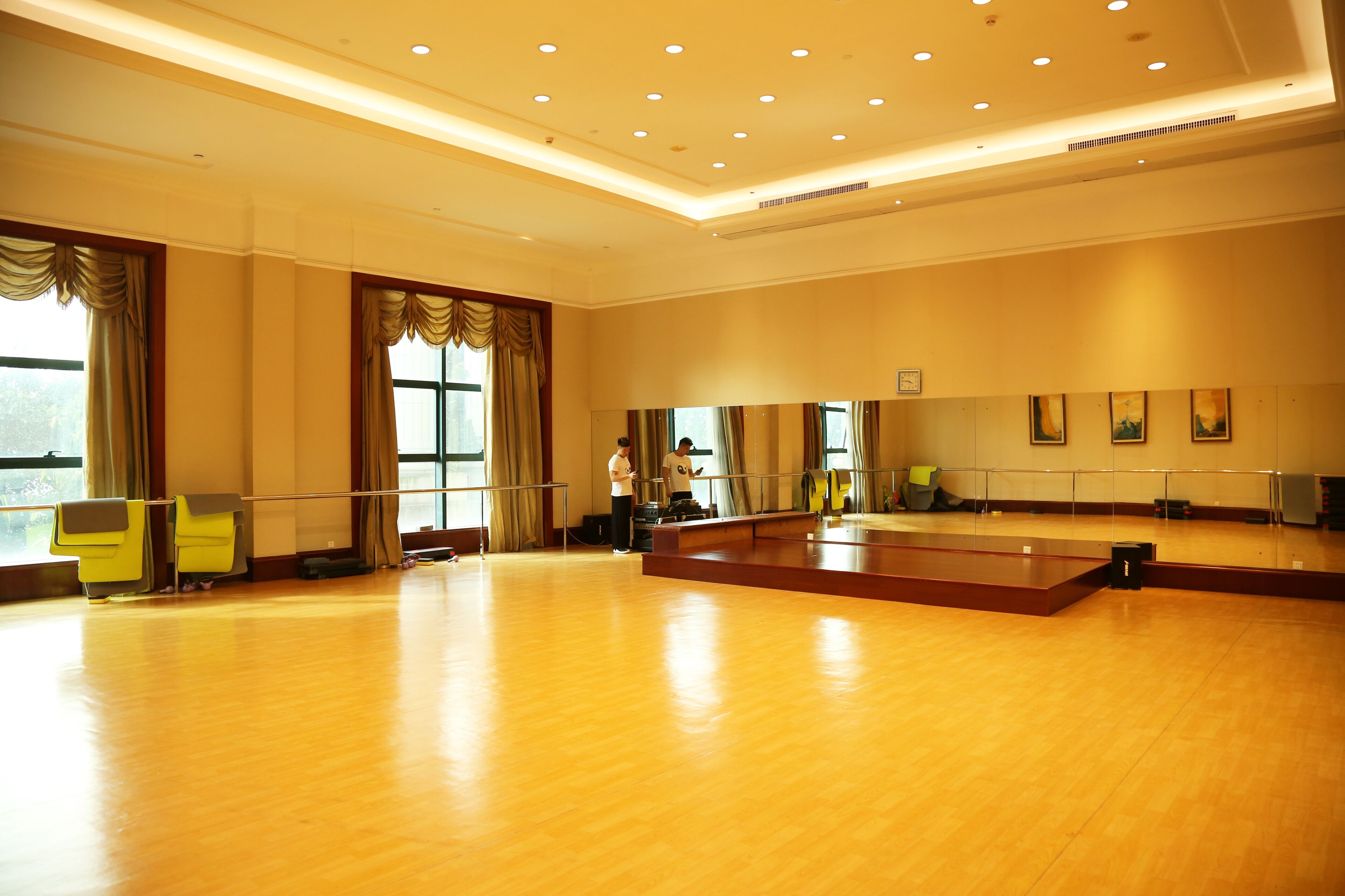A spacious dance studio with a wooden floor, large windows with curtains, and a mirror wall.