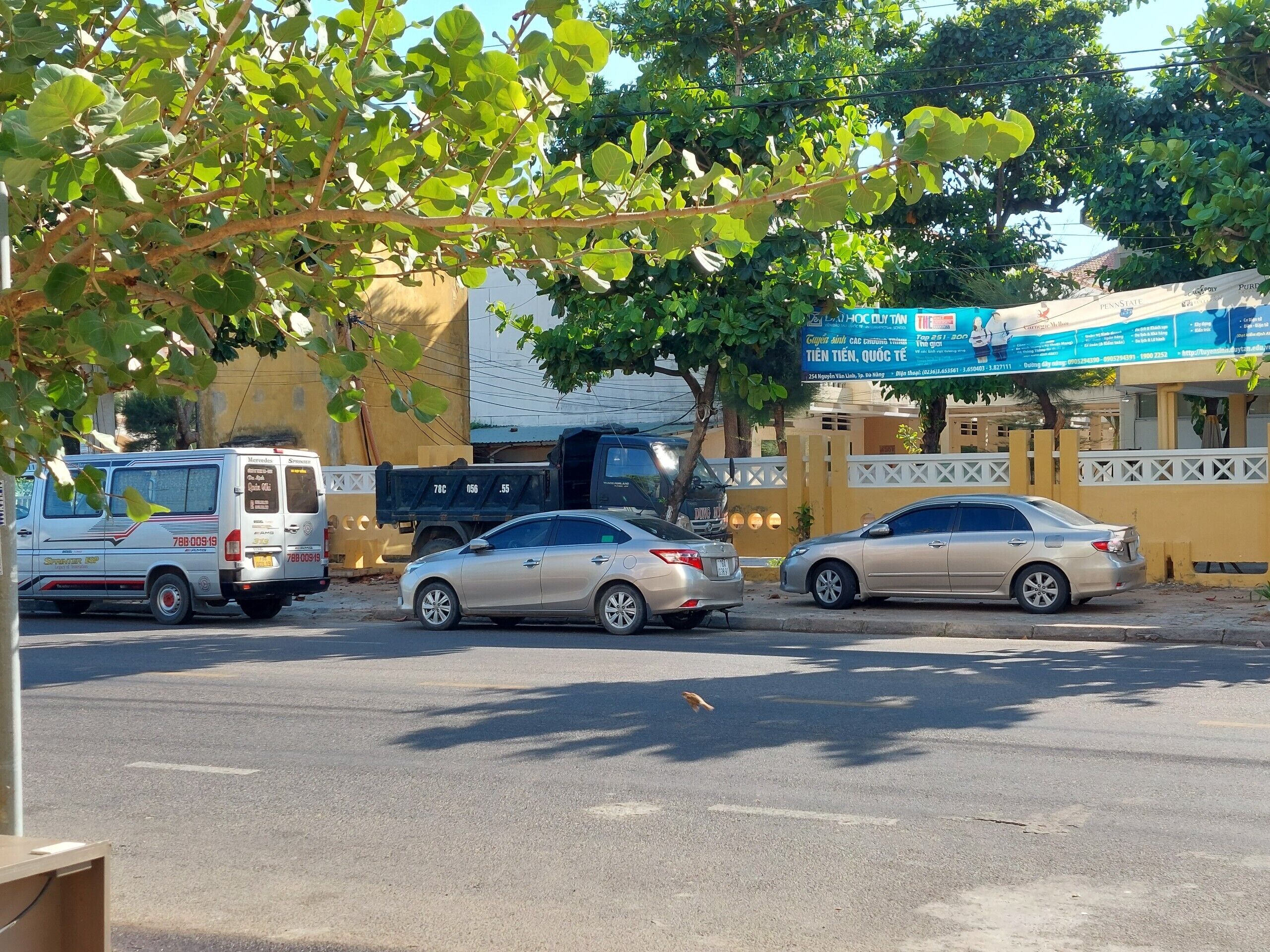 A street scene with parked cars, a truck, and a building with a blue sign.