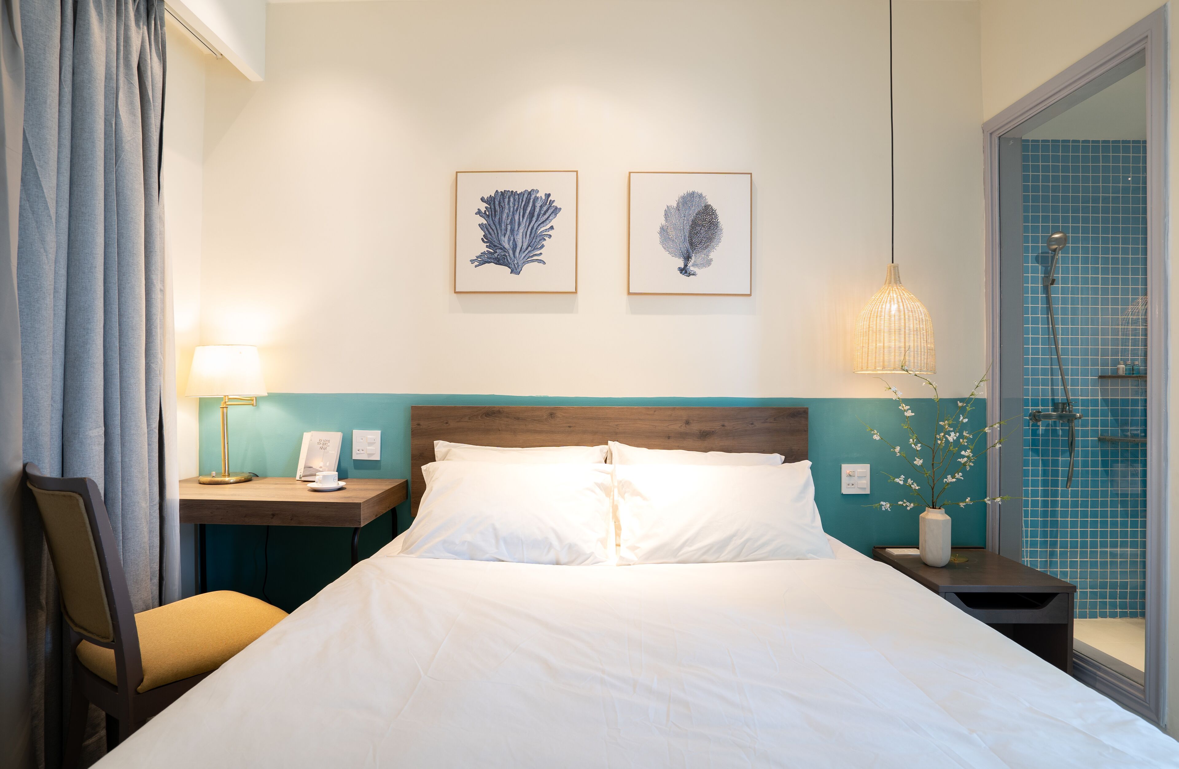 A hotel room with a bed, a nightstand with a lamp, a chair, and two framed pictures on the wall.