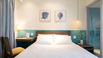 A hotel room with a bed, a nightstand with a lamp, a chair, and two framed pictures on the wall.