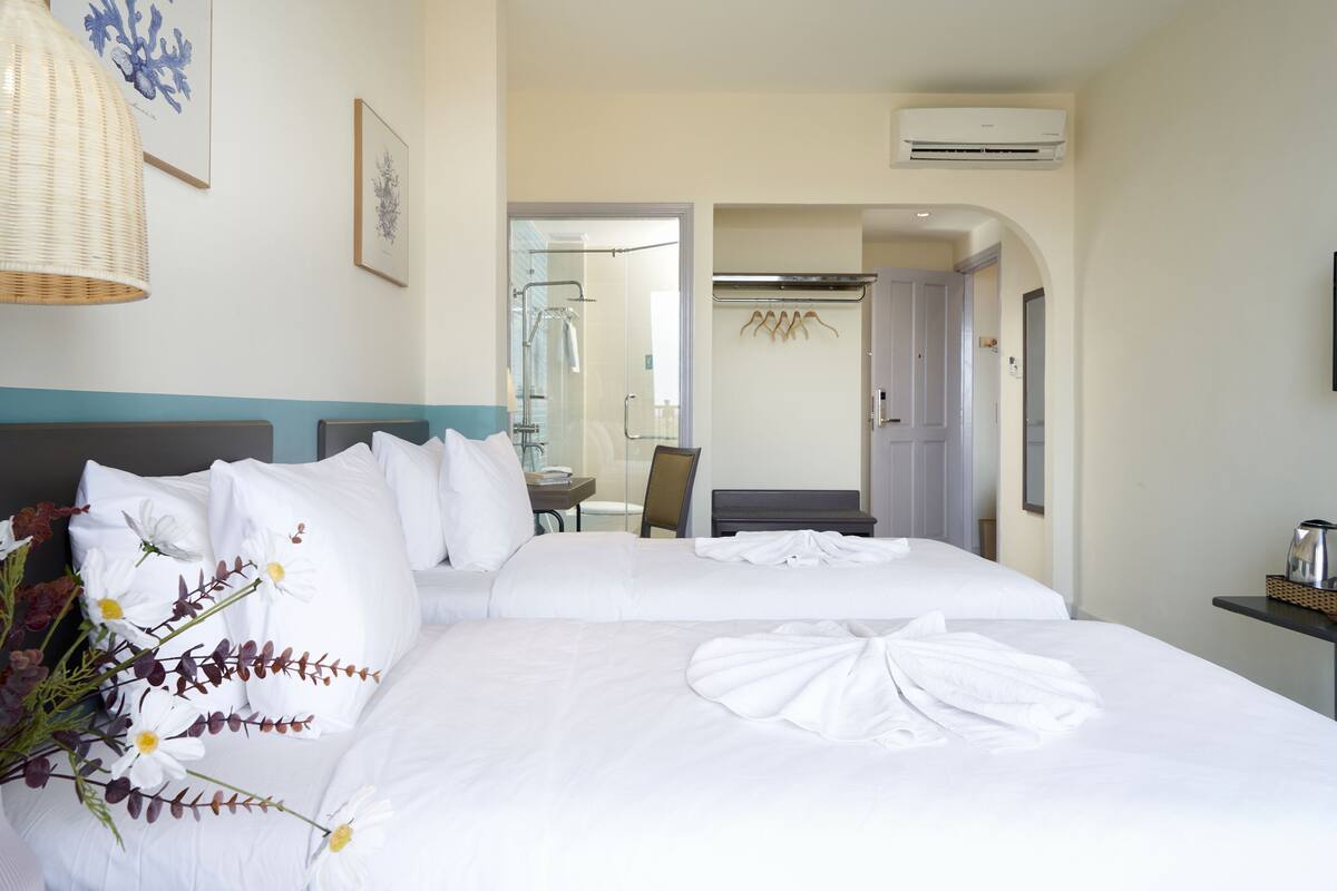 Une chambre d’hôtel avec deux lits, un coin salon avec une table et des chaises, et un espace douche.